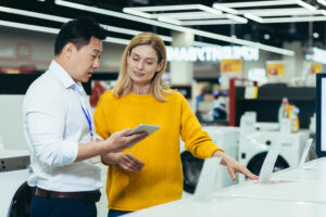 Asian consultant salesman in electronics and household appliances store, selling a working machine to a woman, recommending and approving the choice