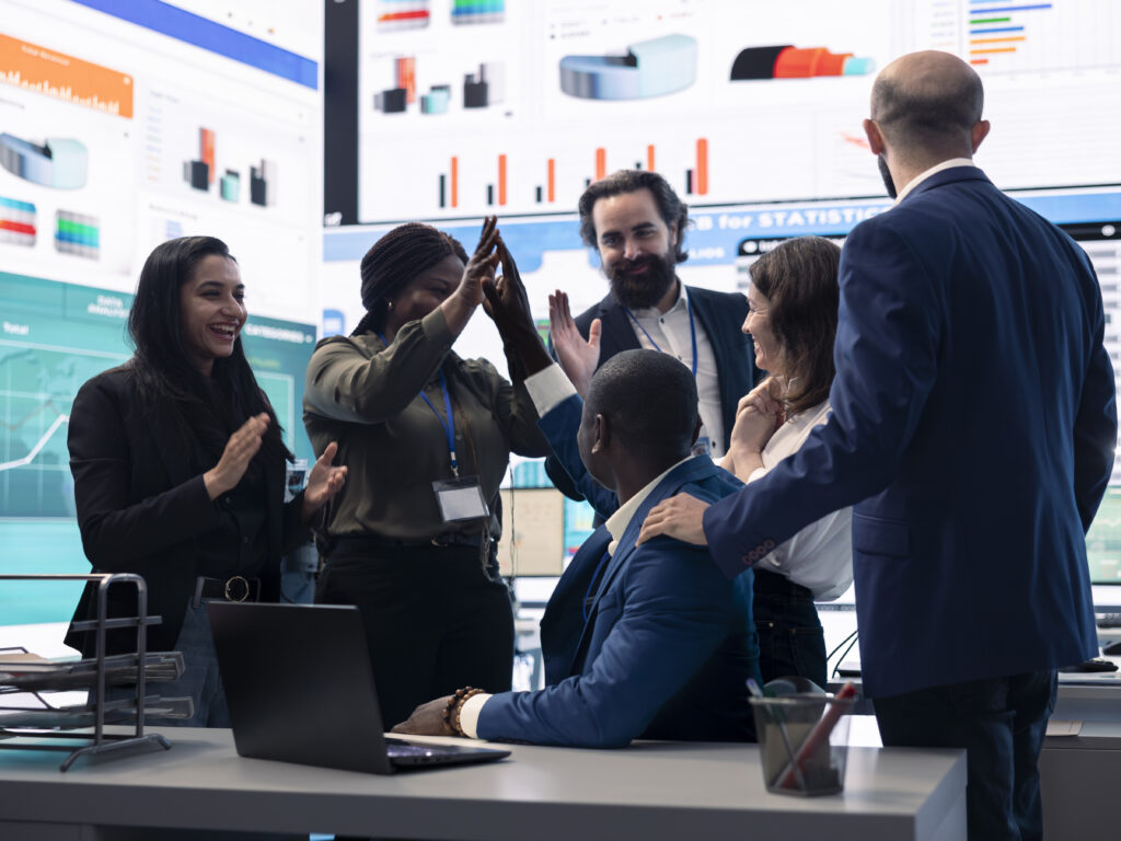 Diverse enterprise team enjoying huge global expansion progress, feeling excited about the future and celebrating a successful partnership outcome. High five between employees.